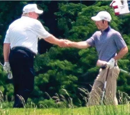  ??  ?? Crisis, what crisis?: President Trump shakes hands with a fellow player during his round of golf