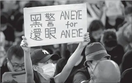  ?? VINCENT THIAN/AP PHOTO ?? A woman holds a placard during Monday’s sit-in protest at the arrival hall of the Hong Kong Internatio­nal Airport. It is reported that police shot a woman in the eye with a projectile Sunday night during confrontat­ions between protesters and police.