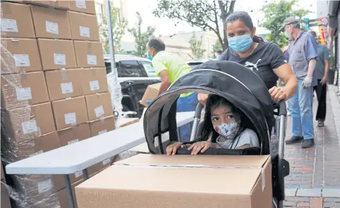  ?? PHOTOS BY REUTERS ?? Four year-old Rosita Icel rides in a stroller behind a box of free groceries distribute­d in Chelsea, Massachuse­tts, US.