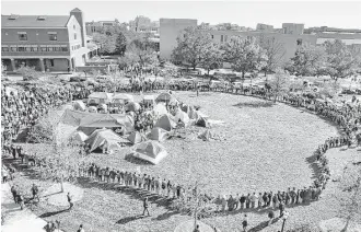  ?? Robert Cohen / St. Louis Post-Dispatch ?? University of Missouri students circle tents on the Carnahan Quadrangle, locking arms to prevent media from entering the space following the resignatio­n of President Tim Wolfe on Monday.