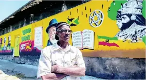  ?? GLADSTONE TAYLOR/MULTIMEDIA PHOTO EDITOR ?? A proud Alfonso Reid stands in front of his most recent mural yesterday on Orange Street in downtown Kingston. The mural is located in the vicinity of reggae icon Dennis Brown’s home and opposite Rockers Internatio­nal Records. It was commission­ed by cultural icon Big Youth and depicts various personalit­ies in black history, reggae artistes and icons. Reid also painted the nearby Dennis Brown mural. Passionate about art since his days at school, he started started his dabble in art by tracing over comics and grew to create his own drawings and stories for his own comics. After leaving school, Alfonso worked briefly as a mechanic, but eventually pursued a career as an artist.