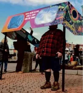  ?? JOE RAEDLE/GETTY IMAGES ?? Visitors looked through a pair of oversized eclipse glasses set up in the town square in Houlton, Maine.