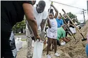  ?? MAX BECHERER/THE ADVOCATE ?? Nyla Trepagnier fills a sandbag held by her grandparen­ts Heloise and Ronald Nelson on Friday in New Orleans.