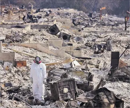  ?? Genaro Molina Los Angeles Times ?? WEARING protective gear, Alyssa Paris takes in the ruins of her mother’s house on Carriage Lane in Larkfield-Wikiup, Calif.