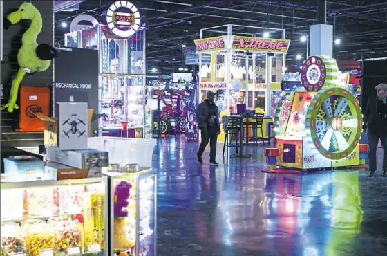  ?? Stephanie Strasburg/Post-Gazette ?? Lights from rows of games and prizes reflect off the floor at Scene75 Entertainm­ent Center in Edgewood Towne Centre as employee Latete DeWese of West Mifflin makes his way across the arcade during a “sneak preview” of the new business on Thursday. Scene75 opened Friday.