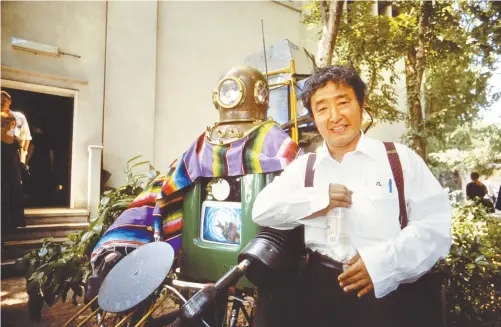  ?? Courtesy of Age Fotostock ?? ◄ Video art visionary Nam June Paik poses with his robot sculpture “Rehabilita­tion of Genghis Khan,” which was unveiled at the 1993 Venice Biennale.