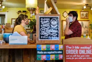  ?? Eli Imadali, Special to The Denver Post ?? A barista and customer wear masks while interactin­g at The Weathervan­e Cafe in July.