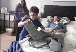  ?? LM OTERO — THE ASSOCIATED PRESS ?? Ronan Kotiya, 11, removes a compressio­n leg sleeve from his father, Rupesh Kotiya, as his mother, Siobhan Pandya, watches at their home in Plano, Texas, on Sunday. Ronan helps care for his father, who suffers from ALS and is dependent on a ventilator.