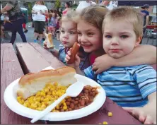  ?? Russ Olivo photo ?? From left, siblings Mia, Makayla and Mason Boucher snuggle at a picnic table as they nosh on hot dogs and corn Monday night on Main Street, courtesy of the Feast of St. Jean Baptiste. An estimated 2,400 individual­s, mostly children, enjoyed a free meal at the event.