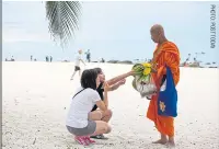  ??  ?? Visitors offer alms to a monk on the beach in Hua Hin.