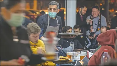  ?? (File Photo/AP/Emilio Morenatti) ?? Waiters wearing masks serve food and drink in a terrace outside Mestalla stadium on March 10, 2020, during the Champions League round of 16 second leg soccer match between Valencia and Atalanta in Valencia, Spain. The match was played in an empty stadium because of the coronaviru­s outbreak.