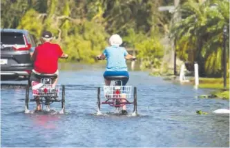  ??  ?? FLORIDA: Two retirees ride tricycles through a flooded street at the Enchanted Shores manufactur­ed home park in Naples, Florida, after Hurricane Irma hit Florida.—AFP