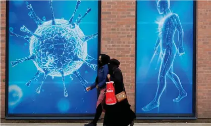  ?? Photograph: Phil Noble/Reuters ?? People walk past an illustrati­on of a virus in Oldham.