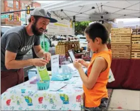  ?? MICHILEA PATTERSON — DIGITAL FIRST MEDIA ?? Daniel Price, Mosaic community garden manger, gives Dylan Bartholome­w, 7, a ground cherry to taste as part of the two-bite club during the weekly outdoor farmers market in Pottstown. Kids that try the product of the month receive a $5 coin that can be...