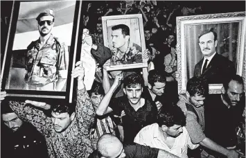  ?? HUSSEIN MALLA/AP 2000 ?? Syrian mourners wave portraits of President Hafez Assad, right, and his sons Bashar, center, and Basil, who died in1994, to mourn the death of Hafez, in Damascus, Syria. Today, Bashar maintains an iron grip on a country that is in ruins.