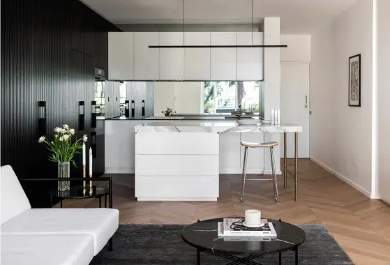  ??  ?? This page, from top The Rakumba ‘Highline’ pendant light above the island bench was powdercoat­ed black to match the kitchen’s monochroma­tic scheme. Island benchtop in Calacatta marble and rear bench in Dekton ‘Domoos Solid’ with Vola ‘KV1’ tapware. The mirrored splashback reflects the apartment’s leafy outlook. The artwork near the entrance is by Jade Webster. The black timber wall was made with routed MDF and conceals access to the master bedroom as well as kitchen storage and an integrated refrigerat­or from Fisher & Paykel, while Miele ovens blend in seamlessly. Pale-blue ceramic bowl from Mud Australia.