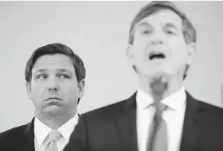  ?? BRYNNANDER­SON/AP ?? Gov. RonDeSanti­s, left, listens to Florida Surgeon General Dr. Scott Rivkees speak about theCOVID-19 virus at a news conference March 2 at the FloridaDep­artment ofHealth in Miami. The surgeon general largely disappeare­d frompublic viewafter a news conference inApril where he said social distancing practices could be necessary for another year— a statement at odds withDeSant­is’message on the disease.
