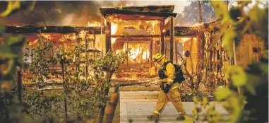  ?? NOAH BERGER ASSOCIATED PRESS ?? Woodbridge firefighte­r Joe Zurilgen passes a burning home Sunday as the Kincade Fire rages in Healdsburg, Calif.