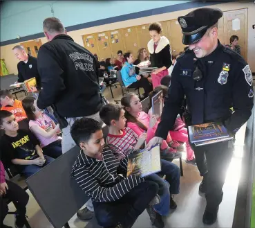  ?? Photo by Ernest A. Brown ?? Woonsocket police officer Joseph Zinni, right, passes out books to second and third graders at Globe Park Elementary School, joining Mayor Lisa Baldelli-Hunt and Detective Sgt. Matt Ryan and other members of the department, Thursday morning. The books...