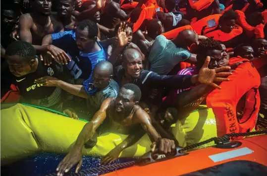  ??  ?? Desperate: Migrants without lifejacket­s scramble to be rescued from the stricken dinghy 15 miles off the Libyan coast