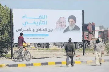  ?? ANMAR KHALIL/AP ?? Iraqis pass a poster announcing the upcoming visit of Pope Francis in Najaf. The pope is scheduled to meet the Grand Ayatollah Ali al-Sistani, right, on Saturday at the cleric’s home. Al-Sistani rarely receives foreign dignitarie­s.