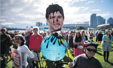  ?? DARRYL DYCK/ THE CANADIAN PRESS ?? A protester holds a photo of Prime Minister Justin Trudeau and a globe covered in oil during a protest against the Kinder Morgan Trans Mountain Pipeline expansion in Vancouver on Tuesday. The government is set to spend $4.5 billion to buy the pipeline.