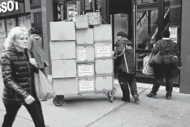  ?? Spencer Platt / Tribune News Service ?? A FedEx worker transports boxes in Manhattan last month. FedEx anticipate­s a busy shipping season and has said it is adding some surcharges for peak season, similar to UPS.