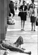  ?? PETER PARKS / AFP / GETTY IMAGES ?? A homeless woman sleeps on the pavement as two office workers approach in Beijing.