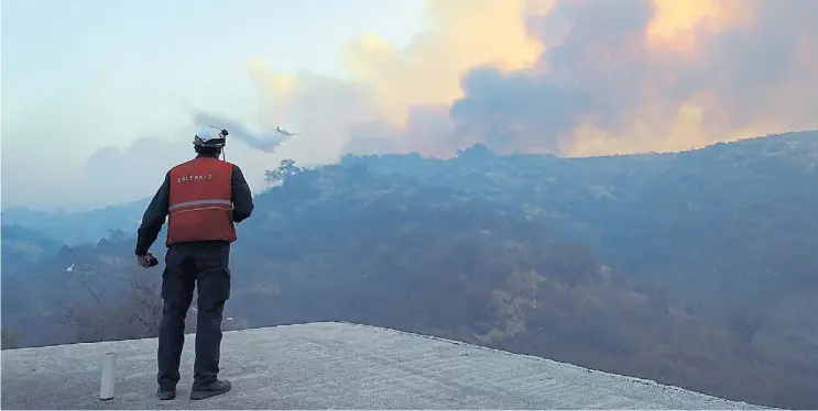  ?? DEFENSA CIVIL ?? Con el clima en contra. Un brigadista observa cómo un avión hidrante combate el fuego en el oeste de Córdoba, donde los vientos son cambiantes y no llueve desde hace varios días.