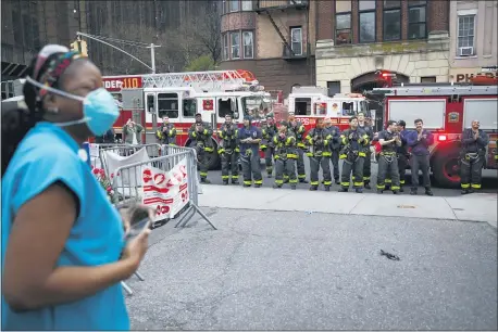  ?? JOHN MINCHILLO — THE ASSOCIATED PRESS FILE ?? In this April 14, 2020, file photo FDNY firefighte­rs gather to applaud medical workers as attending physician Mollie Williams, left, wears personal protective equipment due to COVID-19 concerns outside Brooklyn Hospital Center in New York.