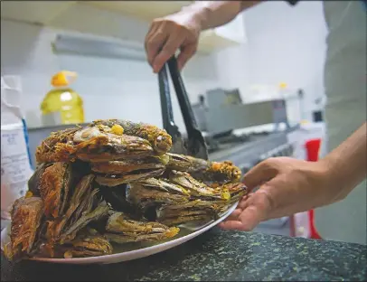  ?? (AP/Jon Gambrell) ?? Gary Dela Pena of Laguna, Philippine­s, puts fried mackerel on a plate June 3 to help Feby Dela Pena feed those who need it in Dubai, United Arab Emirates. Feby Dela Pena, a mother of three, is unemployed, but when she saw people lining up for free meals one night outside her building two weeks ago she decided to use whatever money her family had to help out the countless numbers of Filipinos and others who’ve lost jobs amid the coronaviru­s.