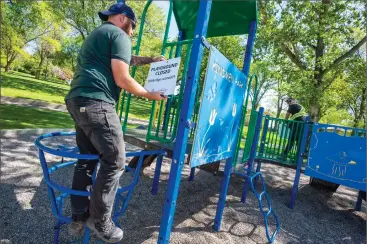  ?? Herald photo by Ian Martens ?? City workers Matt Them and Dylan Beach remove closed signs from a play structure Thursday at Kinsmen Park, as the City prepares to open playground­s today. @IMartensHe­rald