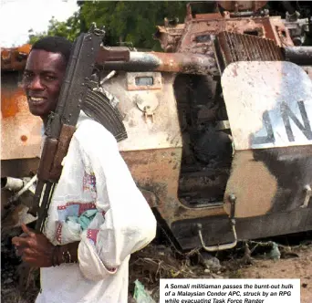  ??  ?? A Somali militiaman passes the burnt-out hulk of a Malaysian Condor APC, struck by an RPG while evacuating Task Force Ranger