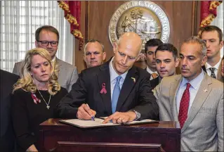  ?? MARK WALLHEISER / ASSOCIATED PRESS ?? Gov. Rick Scott signs the Marjory Stoneman Douglas High School Public Safety Act on Friday at Florida’s Capitol in Tallahasse­e, flanked by victims’ family members: parents Jennifer Montalto (left), Ryan Petty (second from left), Andrew Pollack (right)...