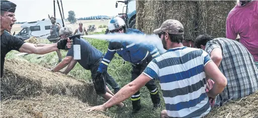  ?? JEFF PACHOUD/AFP/GETTY IMAGES ?? An officer sprays tear gas at protesters as other officials remove hay bales that were used to block the route during Stage 16 of the Tour de France on Tuesday.