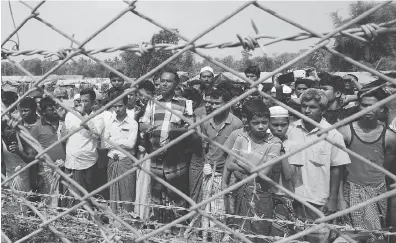  ?? JOE FREEMAN / AFP / GETTY IMAGES ?? Rohingya Muslims gather in March behind Myanmar’s border lined with barbed wire fences in Maungdaw district, located in Rakhine State bounded by Bangladesh.