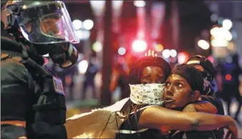  ?? JASON MICZEK / REUTERS ?? Two women embrace while looking at a police officer in Charlotte onWednesda­y during a protest against the police shooting of a black man.