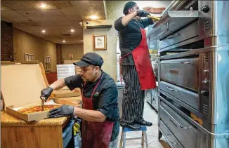  ??  ?? Joanna Fini’s husband Felix Acosta (left) started as a dishwasher. After learning pizza making, he now manages the kitchen. Minding the oven behind him is Andre Ibarra.