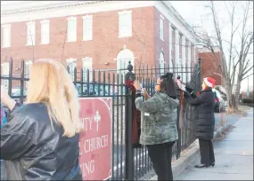  ??  ?? Staff from the Community Health & Wellness Center in Torrington spread warmth in the form of scarves, free for the taking, on fenceposts and street signs near the downtown area earlier this week. Donna Nahajlo “tying one on” the Trinity iron fence