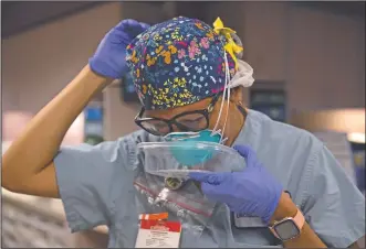  ??  ?? Vargas puts on her N95 mask using a plastic food container while getting ready to assist a covid-19 patient at St. Jude Medical Center. Vargas wears her glasses instead of contacts so she doesn’t have to touch her eyes. She swaps her sneakers out for glittery black clogs so she doesn’t have to handle shoelaces. She seals her N95 mask in a Tupperware-like container between patients so it’s stored away from germs in the air.