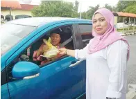  ??  ?? NORAIN menyampaik­an bubur lambuk kepada pengguna jalan raya.