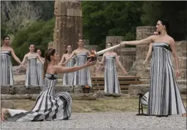  ?? THANASSIS STAVRAKIS — THE ASSOCIATED PRESS ?? Actress Mary Mina, right, playing an ancient Greek priestess, lights a torch Tuesday during the official ceremony of the flame lighting for the Paris Olympics.