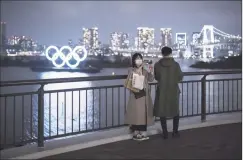  ?? Getty Images ?? A woman wearing a face mask uses a smartphone as she takes a photograph in front of the Olympic rings Wednesday in Tokyo.