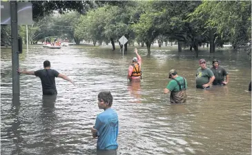  ??  ?? Volunteer and rescue officials wait to help residents to safety after they had to be rescued by boats from their homes after the area flooded in Houston. Forecasts on Tuesday called for still more rain, making clear that catastroph­ic flooding was just...