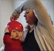  ?? DAVID GOLDMAN — ASSOCIATED PRESS ?? Chesla Whitt, right, takes off a helmet her nine-month old son, Tommy Joe, must wear after being born with a rare condition where his skull bones didn’t fuse together properly, at their home in Sandy Hook, Ky., earlier this month.