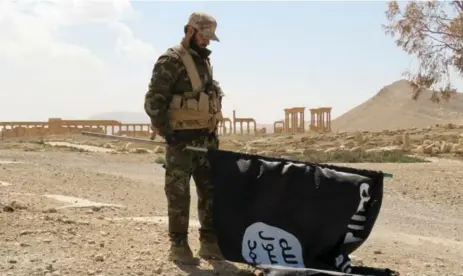  ?? AFP/GETTY IMAGES ?? A pro-government Syrian fighter carries a captured Daesh flag after the ancient city of Palmyra was recaptured last weekend.