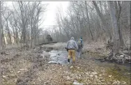  ?? NWA Democrat-Gazette/Flip Putthoff ?? Chris Denham (left) and Gary Wellesley follow Spec across a creek on the hunt for squirrels.