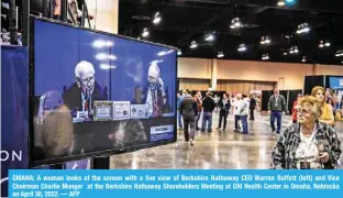  ?? — AFP ?? OMAHA: A woman looks at the screen with a live view of Berkshire Hathaway CEO Warren Buffett (left) and Vice Chairman Charlie Munger at the Berkshire Hathaway Shareholde­rs Meeting at CHI Health Center in Omaha, Nebraska on April 30, 2022.