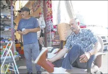  ?? Erik Verduzco Las Vegas Review-Journal ?? Vendor Javier Rivas, left, assists Pedro Ortega in his quest for a pair of boots.
