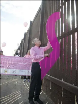  ?? VINCENT OSUNA PHOTO ?? Consul of México Carlos Flores Vizcarra holds half of a cutout pink ribbon against the border fence while Mujeres Que Viven members in Mexicali hold another cutout, creating a complete ribbon during the sixth annual Lazo Rosa Binacional walk in...